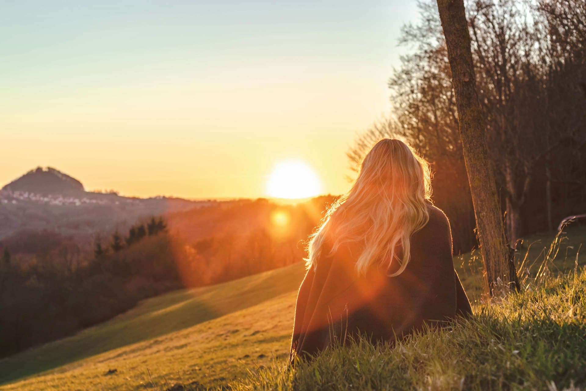 A woman sitting on a hillside at golden hour, gazing peacefully over a valley